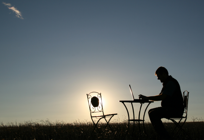 man sitting outside on a laptop at a bistro table